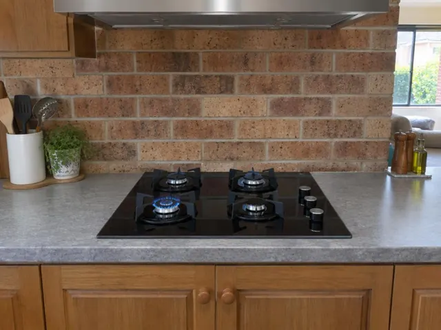 Black gas cooktop set into a stone-look benchtop with brick splashback in a home kitchen in Windale