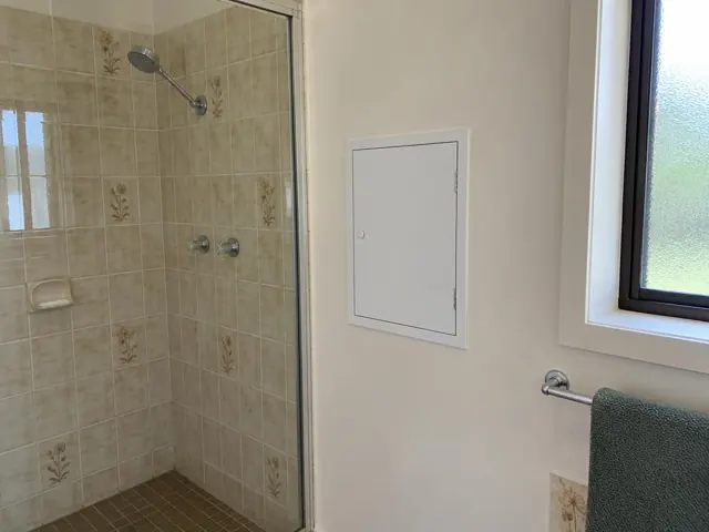 Bathroom shower wall with a small access panel beside a window in Windale
