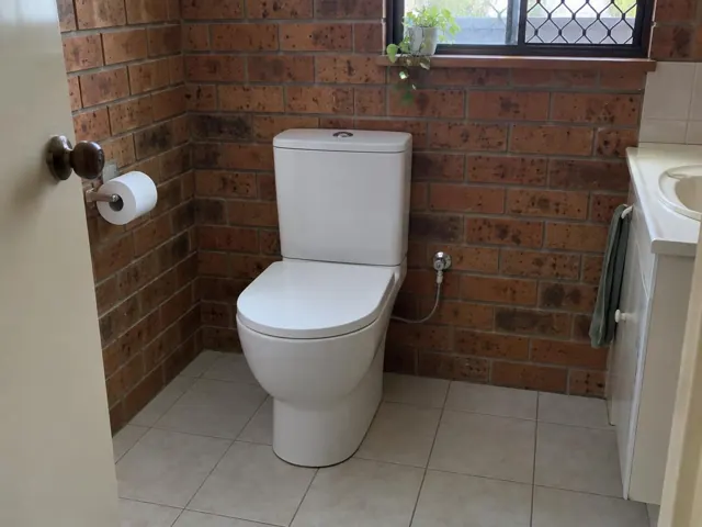 White toilet in a brick-walled bathroom with tiled floor and window in Gateshead